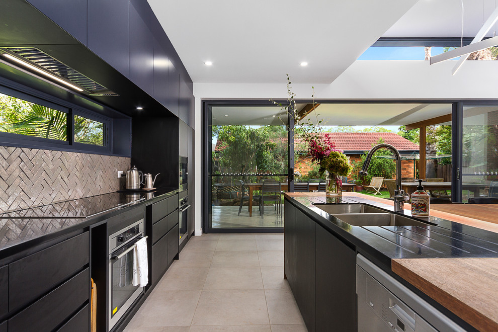 Mid-sized contemporary galley open plan kitchen in Sydney with an undermount sink, flat-panel cabinets, black cabinets, wood benchtops, green splashback, ceramic splashback, stainless steel appliances, cement tiles, with island and grey floor.