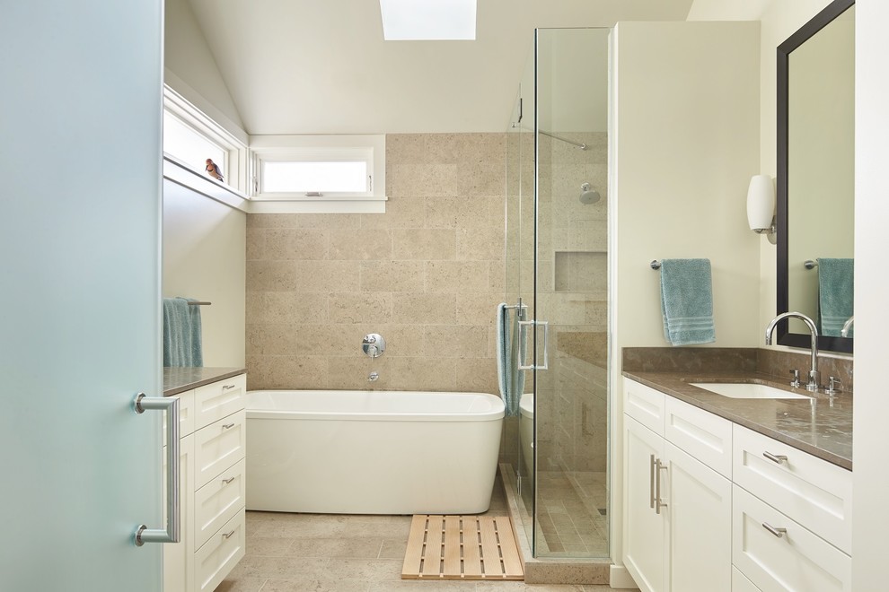 Inspiration for a mid-sized modern master bathroom in Seattle with an undermount sink, recessed-panel cabinets, white cabinets, limestone benchtops, a freestanding tub, a corner shower, a one-piece toilet, gray tile, stone slab, white walls and limestone floors.