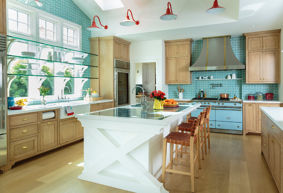 This is an example of an expansive beach style u-shaped eat-in kitchen in Los Angeles with a farmhouse sink, shaker cabinets, marble benchtops, blue splashback, cement tile splashback, with island, brown floor, medium wood cabinets, coloured appliances, medium hardwood floors and white benchtop.