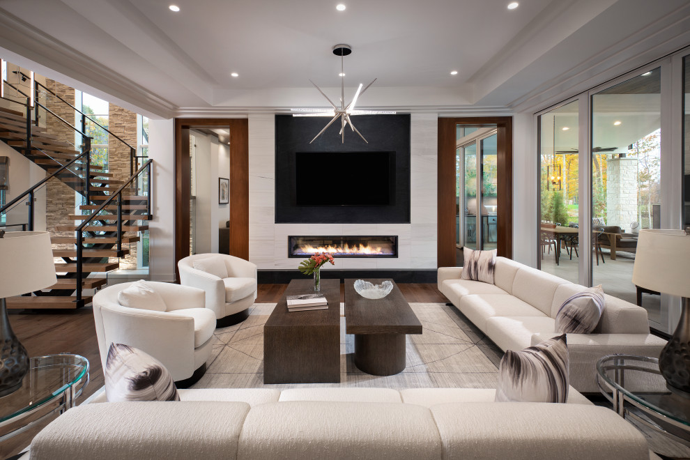 Expansive contemporary open concept living room in Nashville with white walls, medium hardwood floors, a standard fireplace, a tile fireplace surround, a built-in media wall and recessed.