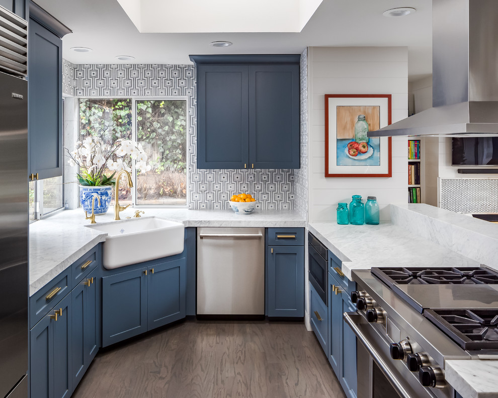 Photo of a mid-sized transitional u-shaped kitchen in San Diego with a farmhouse sink, recessed-panel cabinets, blue cabinets, granite benchtops, grey splashback, ceramic splashback, stainless steel appliances, dark hardwood floors and no island.