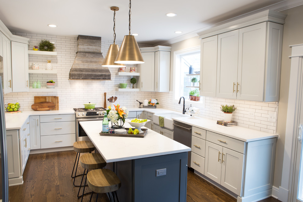 Photo of a mid-sized transitional u-shaped eat-in kitchen in Chicago with a farmhouse sink, shaker cabinets, quartz benchtops, white splashback, subway tile splashback, stainless steel appliances, medium hardwood floors, with island, brown floor and white benchtop.