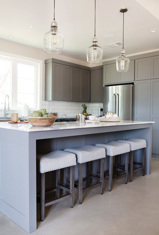 Inspiration for a large transitional l-shaped concrete floor and gray floor eat-in kitchen remodel in Austin with shaker cabinets, gray cabinets, marble countertops, white backsplash, subway tile backsplash, stainless steel appliances, an island and a farmhouse sink