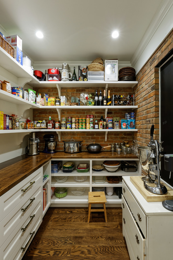 Photo of a traditional l-shaped kitchen pantry in Cincinnati with white cabinets, wood benchtops, brick splashback, dark hardwood floors, brown floor and brown benchtop.