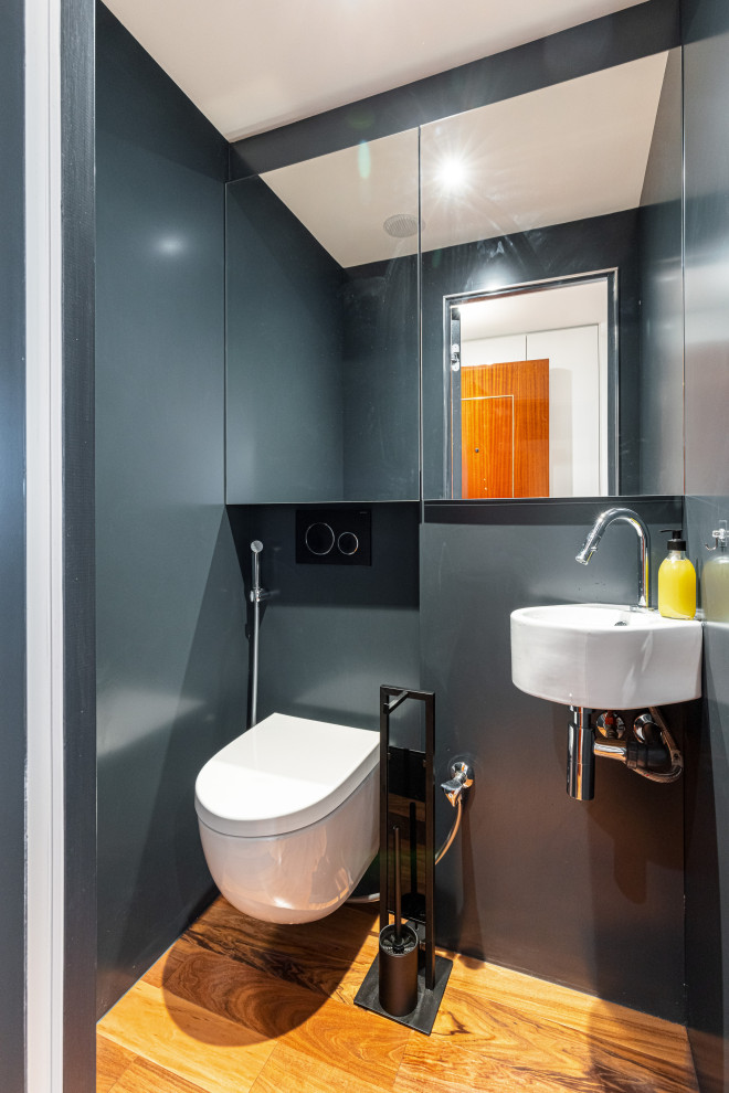 Cette image montre un WC suspendu traditionnel de taille moyenne avec un placard à porte vitrée, un carrelage gris, un mur gris, un sol en bois brun, un lavabo suspendu, un sol beige et meuble-lavabo suspendu.