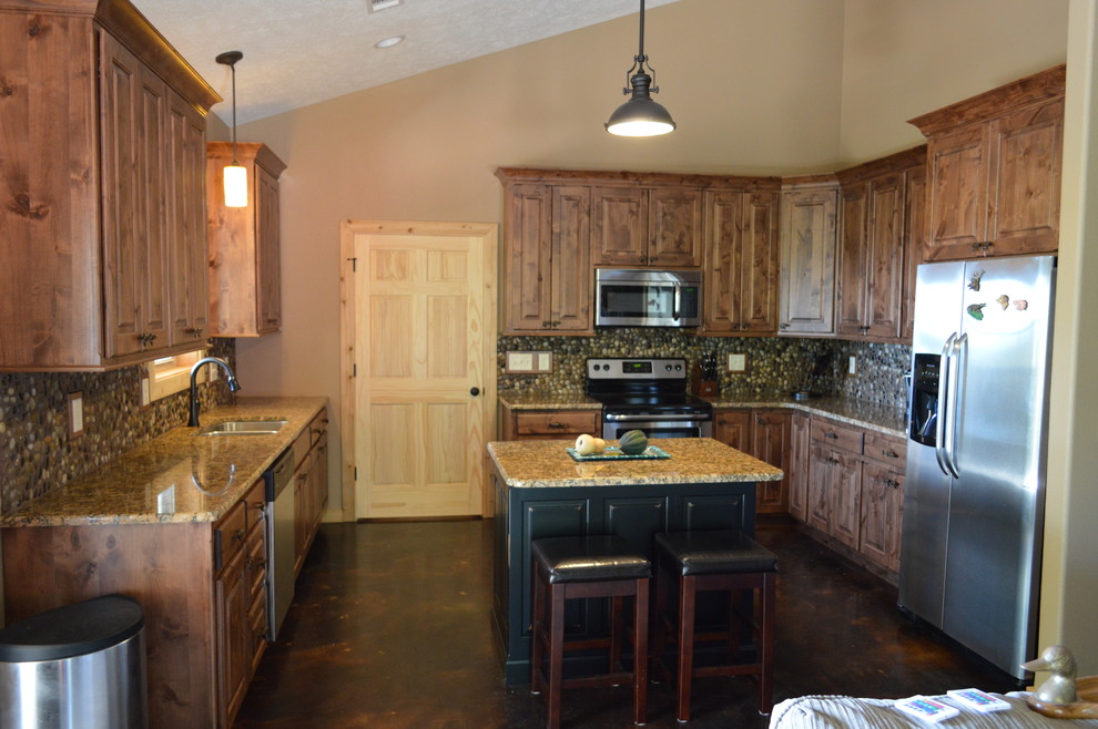 Mountain style concrete floor kitchen photo with an undermount sink, brown cabinets, granite countertops, multicolored backsplash, stainless steel appliances and an island