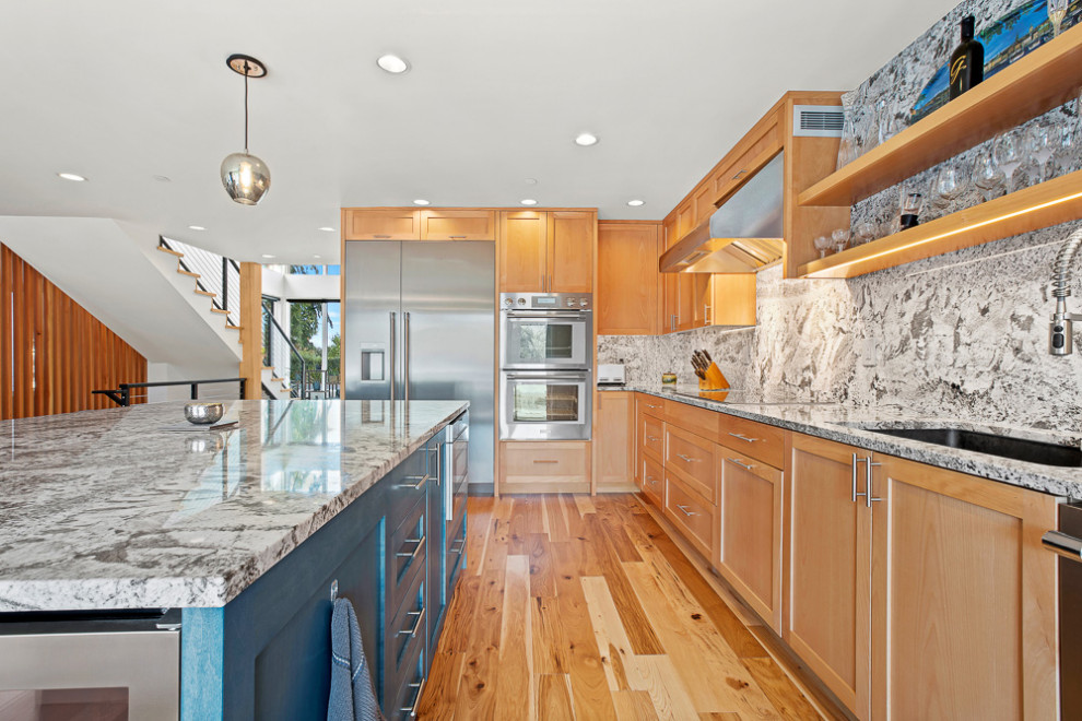 This is an example of a mid-sized transitional l-shaped open plan kitchen in Seattle with an undermount sink, shaker cabinets, medium wood cabinets, granite benchtops, grey splashback, granite splashback, stainless steel appliances, medium hardwood floors, with island and grey benchtop.