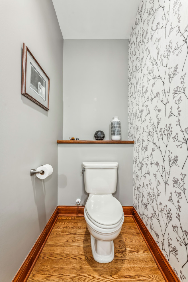 Powder room - small traditional medium tone wood floor and wallpaper powder room idea in Columbus with recessed-panel cabinets, black cabinets, a two-piece toilet, gray walls, a vessel sink, quartz countertops, gray countertops and a built-in vanity
