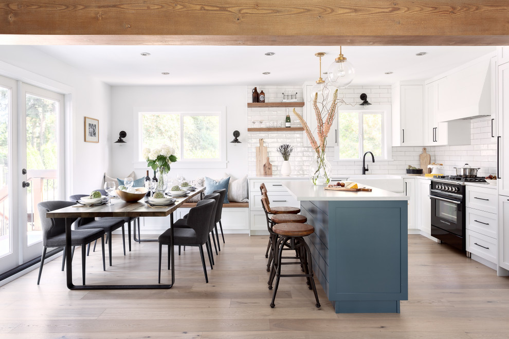 This is an example of a mid-sized country l-shaped eat-in kitchen in Vancouver with a farmhouse sink, shaker cabinets, white cabinets, white splashback, light hardwood floors, with island, beige floor, white benchtop and exposed beam.