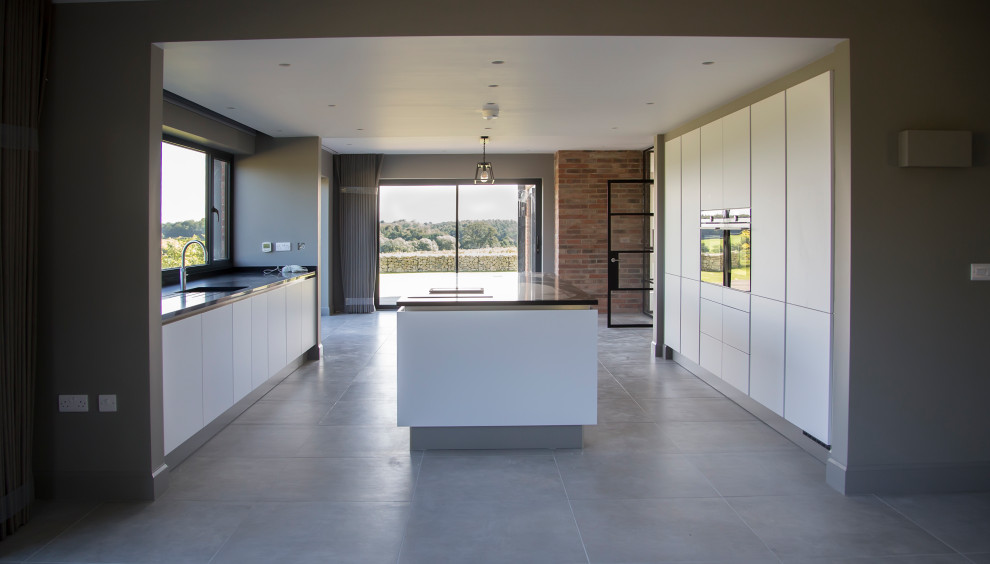 Photo of a large contemporary single-wall open plan kitchen in Other with a double-bowl sink, flat-panel cabinets, white cabinets, quartzite benchtops, black splashback, granite splashback, stainless steel appliances, ceramic floors, with island, grey floor and black benchtop.
