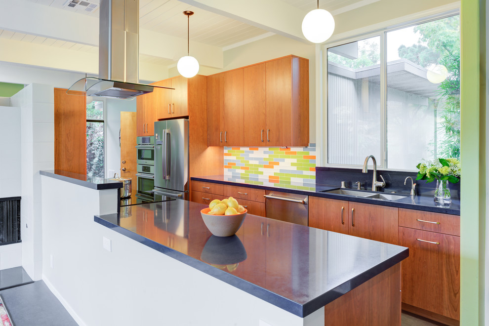 This is an example of a midcentury galley kitchen in San Francisco with flat-panel cabinets, quartz benchtops, multi-coloured splashback, stainless steel appliances, a double-bowl sink, medium wood cabinets, a peninsula and grey benchtop.