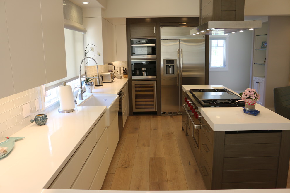 Photo of a mid-sized contemporary u-shaped open plan kitchen in San Francisco with a farmhouse sink, flat-panel cabinets, white cabinets, quartzite benchtops, white splashback, subway tile splashback, stainless steel appliances, light hardwood floors and with island.