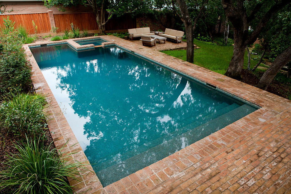 This is an example of a mid-sized midcentury backyard rectangular lap pool in Austin with brick pavers and a hot tub.