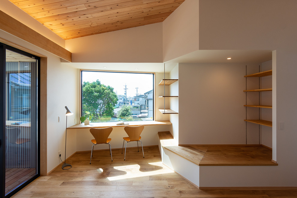 Foto på ett stort minimalistiskt hemmabibliotek, med vita väggar, mellanmörkt trägolv och ett inbyggt skrivbord