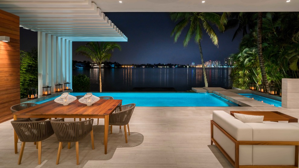 Design ideas for a large contemporary backyard patio in Miami with tile and a roof extension.