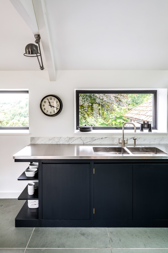 Photo of a large contemporary l-shaped open plan kitchen in Other with an integrated sink, flat-panel cabinets, black cabinets, stainless steel benchtops, white splashback, marble splashback, stainless steel appliances, with island and grey floor.