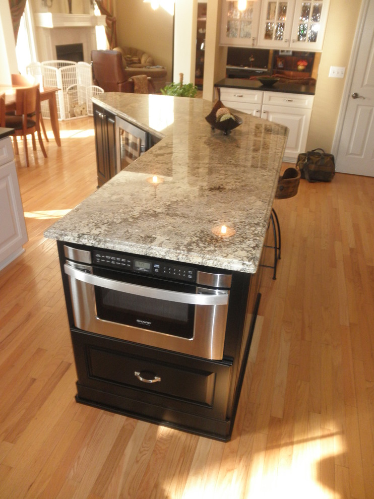 Example of a minimalist l-shaped light wood floor home design design with an undermount sink, raised-panel cabinets, white cabinets, granite countertops, yellow backsplash, stone tile backsplash, stainless steel appliances, beige walls and an island