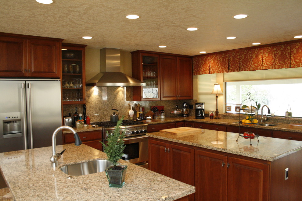 Inspiration for a large traditional u-shaped eat-in kitchen in Sacramento with granite benchtops, multiple islands, an undermount sink, raised-panel cabinets, dark wood cabinets, stone slab splashback, stainless steel appliances and light hardwood floors.