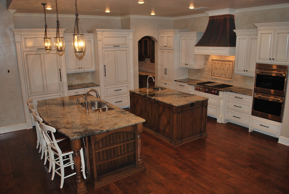 Inspiration for a transitional l-shaped medium tone wood floor and brown floor eat-in kitchen remodel with an undermount sink, raised-panel cabinets, white cabinets, granite countertops, travertine backsplash, paneled appliances and two islands