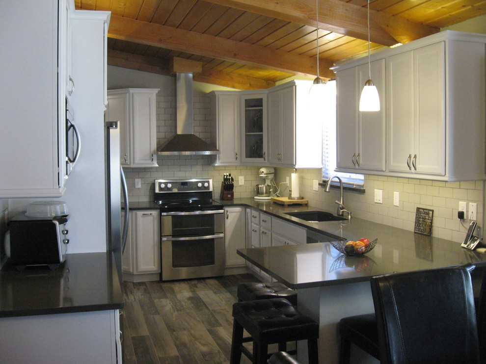 Inspiration for a mid-sized transitional u-shaped dark wood floor and brown floor kitchen remodel in Denver with an undermount sink, white cabinets, quartz countertops, white backsplash, subway tile backsplash, stainless steel appliances, a peninsula and gray countertops