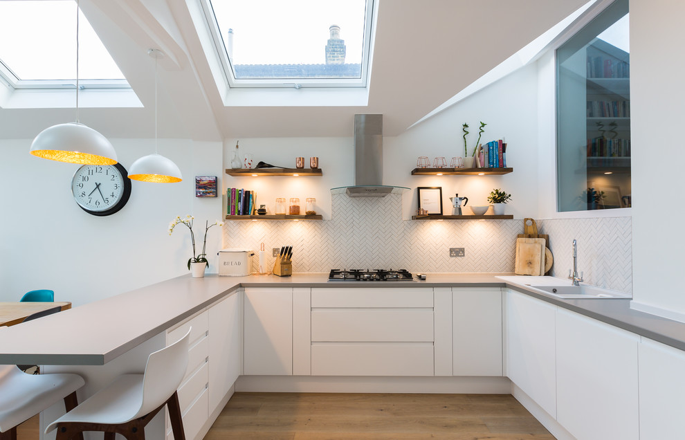 Photo of a contemporary u-shaped kitchen in London with a drop-in sink, flat-panel cabinets, white cabinets, white splashback, mosaic tile splashback, medium hardwood floors, a peninsula, brown floor and grey benchtop.