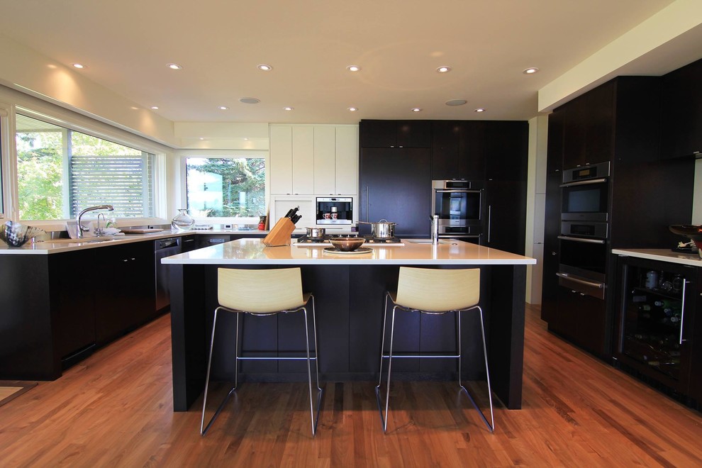 Large transitional u-shaped medium tone wood floor kitchen photo in Calgary with an undermount sink, flat-panel cabinets, black cabinets, solid surface countertops, stainless steel appliances and an island