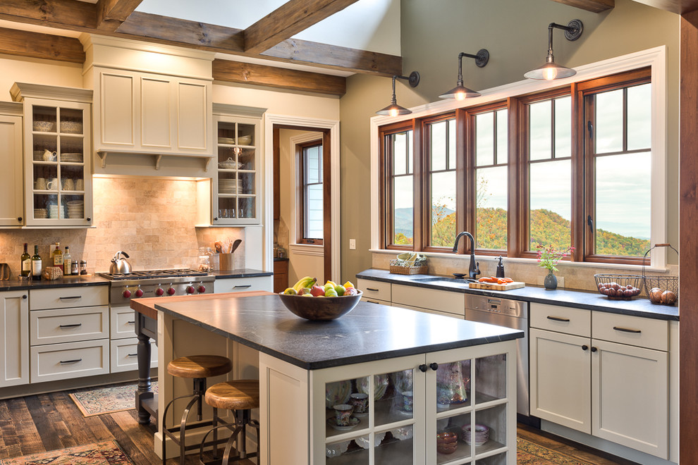 This is an example of a country eat-in kitchen in Other with soapstone benchtops, multiple islands, an undermount sink, white cabinets, stone tile splashback, stainless steel appliances and dark hardwood floors.