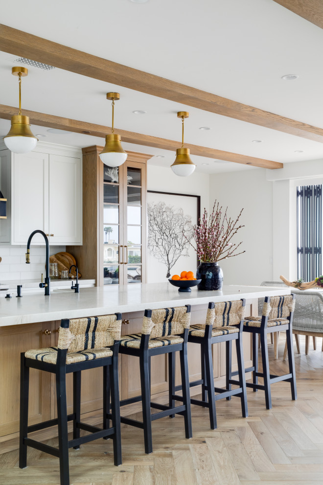 Foto di un cucina con isola centrale stile marino con ante in legno chiaro, top in marmo, elettrodomestici in acciaio inossidabile, parquet chiaro e travi a vista
