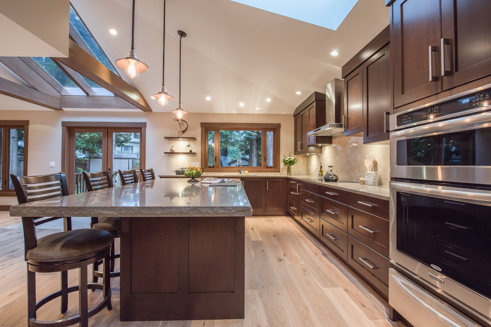 Inspiration for a large country l-shaped open plan kitchen in Vancouver with an undermount sink, recessed-panel cabinets, dark wood cabinets, quartz benchtops, beige splashback, stainless steel appliances, light hardwood floors and with island.
