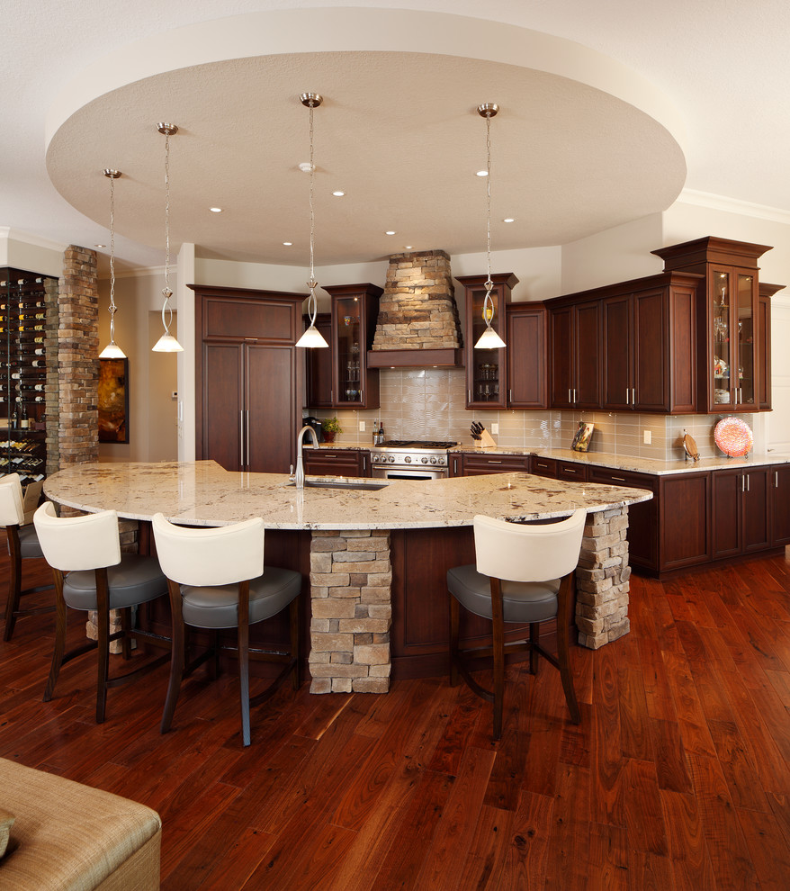 This is an example of a traditional l-shaped eat-in kitchen in Orlando with an undermount sink, raised-panel cabinets, dark wood cabinets, granite benchtops, beige splashback, brick splashback, stainless steel appliances, dark hardwood floors, multiple islands and brown floor.