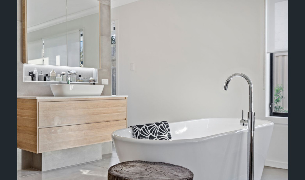 This is an example of a mid-sized contemporary master bathroom in Gold Coast - Tweed with flat-panel cabinets, light wood cabinets, a freestanding tub, an alcove shower, a one-piece toilet, beige tile, ceramic tile, white walls, ceramic floors, a vessel sink, engineered quartz benchtops, beige floor, an open shower, white benchtops, a single vanity and a floating vanity.