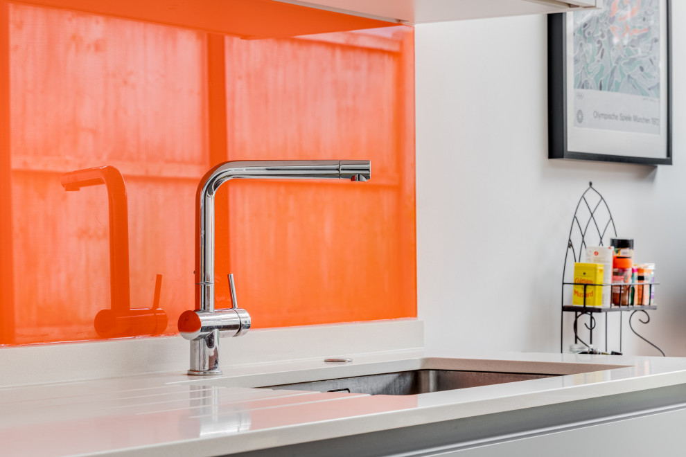 Bild på ett stort funkis vit vitt kök och matrum, med en nedsänkt diskho, grå skåp, bänkskiva i kvartsit, orange stänkskydd, glaspanel som stänkskydd, färgglada vitvaror, ljust trägolv och brunt golv