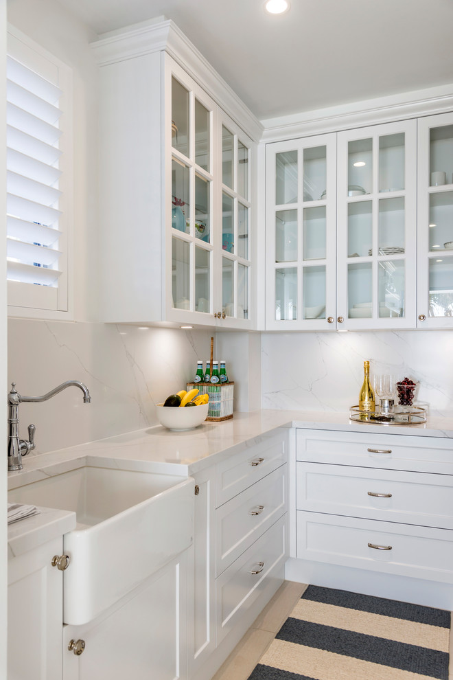 This is an example of a large beach style galley eat-in kitchen in Gold Coast - Tweed with a farmhouse sink, shaker cabinets, white cabinets, marble benchtops, white splashback, marble splashback, stainless steel appliances, ceramic floors, with island, beige floor and white benchtop.