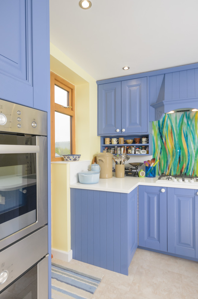 Small eclectic open plan kitchen in Manchester with blue cabinets, wood benchtops, multi-coloured splashback, glass sheet splashback and laminate floors.