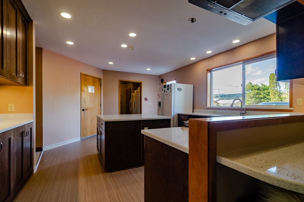 Example of a large transitional u-shaped light wood floor and beige floor enclosed kitchen design with an undermount sink, recessed-panel cabinets, dark wood cabinets, quartz countertops, stainless steel appliances, an island and white countertops