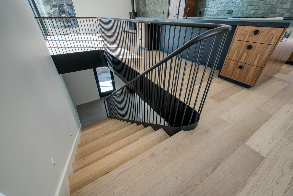Идея дизайна: изогнутая деревянная лестница в современном стиле с деревянными ступенями и металлическими перилами