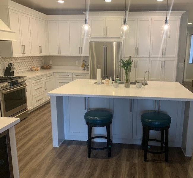 Example of a mid-sized transitional u-shaped laminate floor eat-in kitchen design in Phoenix with a farmhouse sink, shaker cabinets, white cabinets, quartz countertops, gray backsplash, porcelain backsplash, stainless steel appliances, an island and white countertops