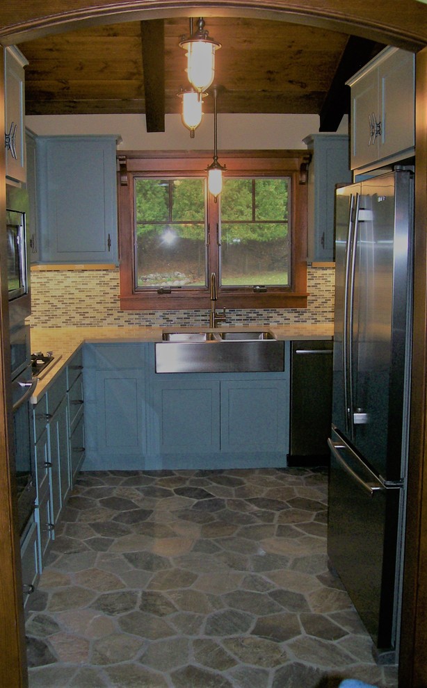 Example of a mid-sized mountain style u-shaped vinyl floor enclosed kitchen design with shaker cabinets, blue cabinets, no island, a farmhouse sink, limestone countertops, multicolored backsplash, glass tile backsplash and stainless steel appliances