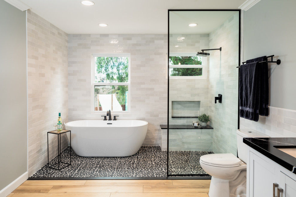This is an example of a traditional wet room bathroom in San Diego with a freestanding bath, white tiles, grey walls, pebble tile flooring, a submerged sink, black floors, black worktops, a wall niche and a shower bench.