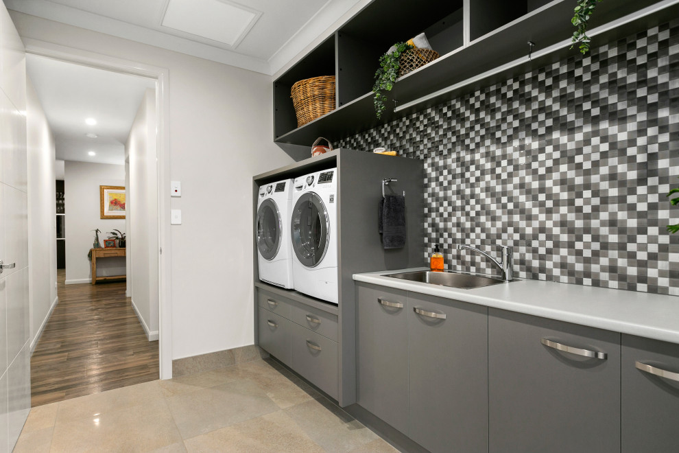 Inspiration for a contemporary single-wall dedicated laundry room in Other with a drop-in sink, flat-panel cabinets, grey cabinets, white walls, a side-by-side washer and dryer, beige floor and grey benchtop.