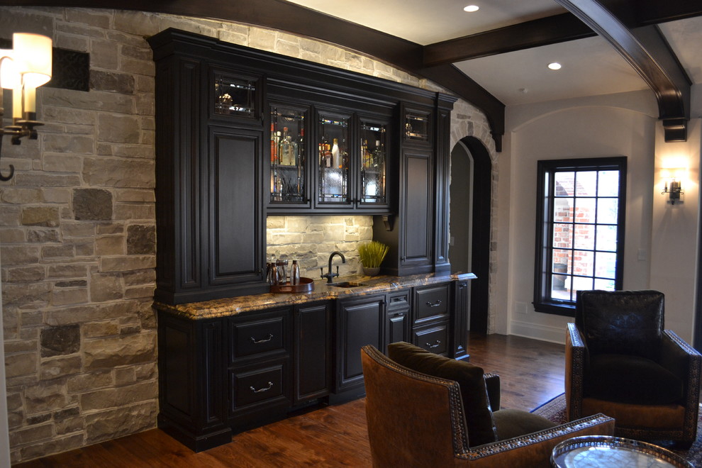 Design ideas for a mid-sized traditional single-wall wet bar in St Louis with an undermount sink, raised-panel cabinets, black cabinets, grey splashback, stone tile splashback, granite benchtops, dark hardwood floors and brown floor.