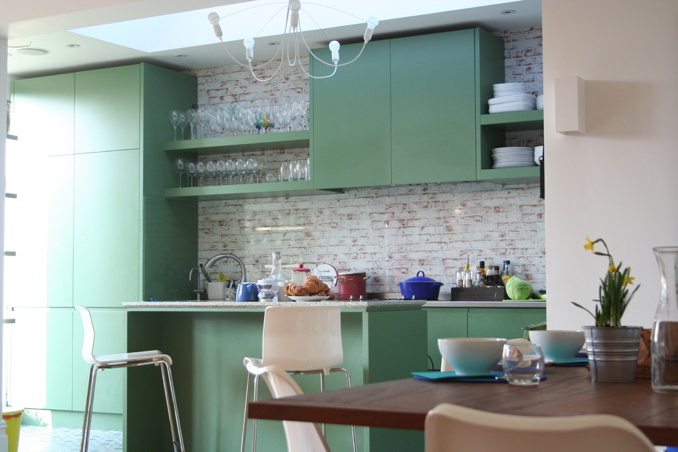 Medium sized classic single-wall open plan kitchen in London with an integrated sink, flat-panel cabinets, green cabinets, stainless steel worktops, multi-coloured splashback, glass sheet splashback, ceramic flooring and an island.
