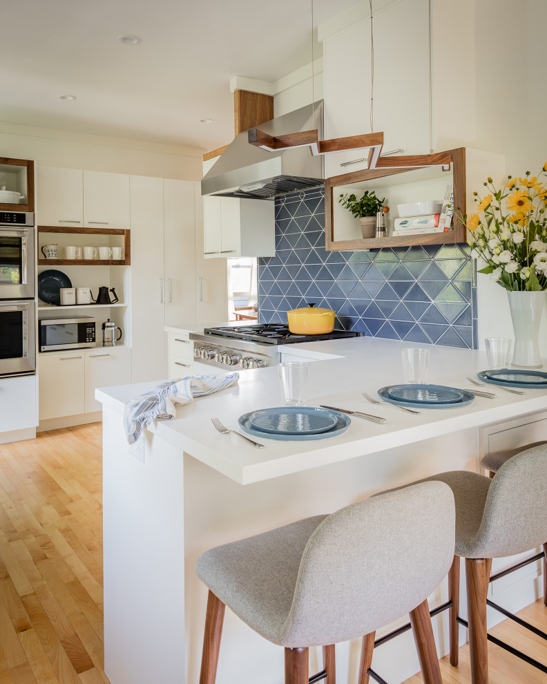 Design ideas for a mid-sized contemporary l-shaped separate kitchen in Boston with an undermount sink, flat-panel cabinets, white cabinets, solid surface benchtops, blue splashback, ceramic splashback, stainless steel appliances, light hardwood floors, a peninsula and white benchtop.