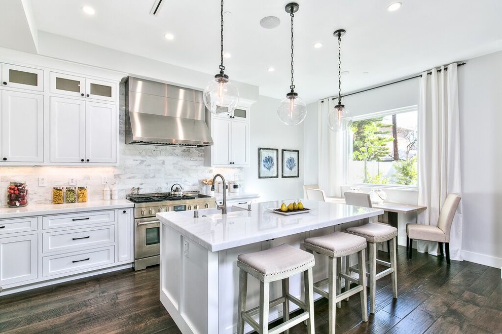 Large transitional l-shaped dark wood floor and brown floor eat-in kitchen photo in Orange County with a farmhouse sink, shaker cabinets, white cabinets, marble countertops, white backsplash, marble backsplash, stainless steel appliances and an island