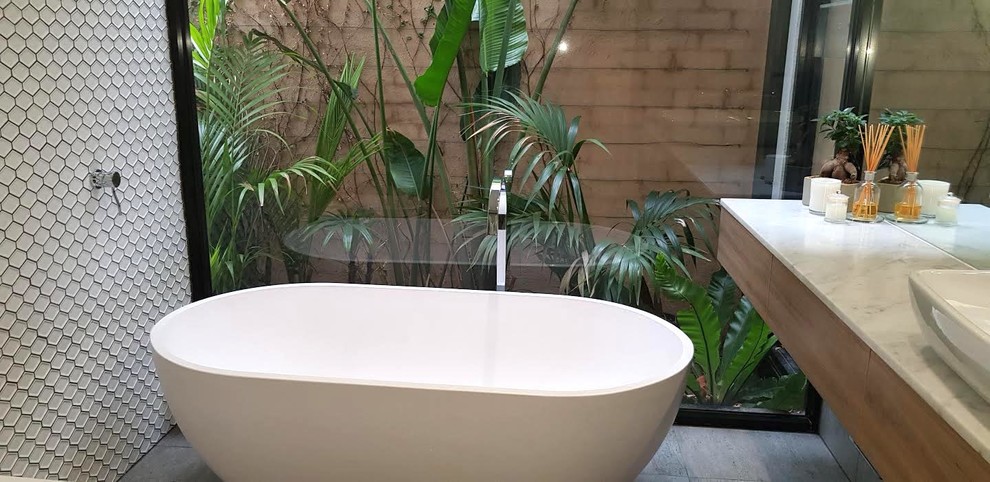 This is an example of a mid-sized modern master bathroom with a freestanding tub, an open shower, a one-piece toilet, white tile, cement tile, white walls, cement tiles, marble benchtops, grey floor, an open shower and white benchtops.