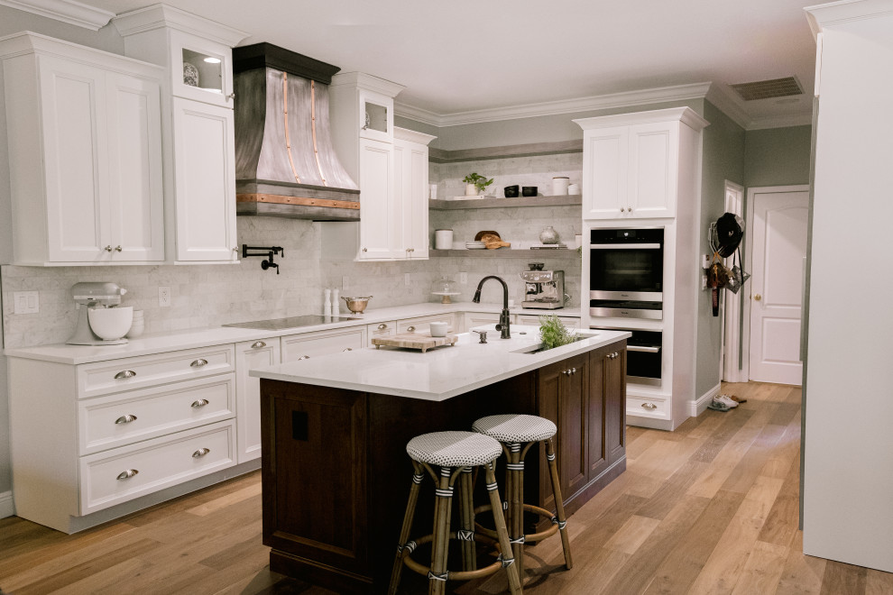 Inspiration for a large transitional l-shaped laminate floor and brown floor kitchen pantry remodel in Orlando with a farmhouse sink, recessed-panel cabinets, white cabinets, quartz countertops, gray backsplash, black appliances, an island and white countertops