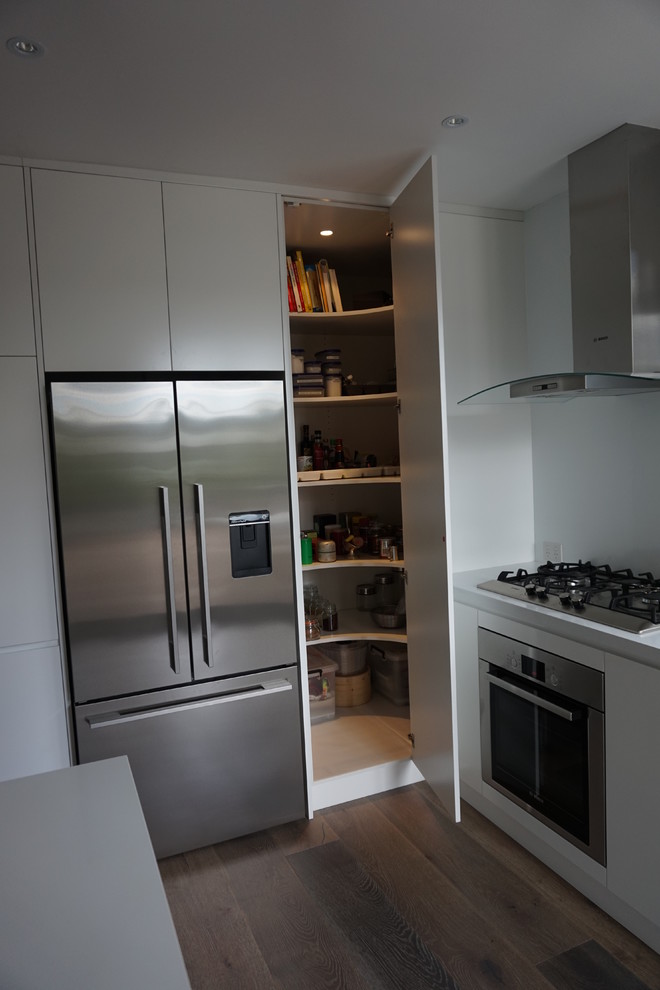 Photo of a mid-sized modern l-shaped eat-in kitchen in Sydney with an undermount sink, flat-panel cabinets, white cabinets, quartz benchtops, white splashback, stainless steel appliances, ceramic floors, with island and glass sheet splashback.