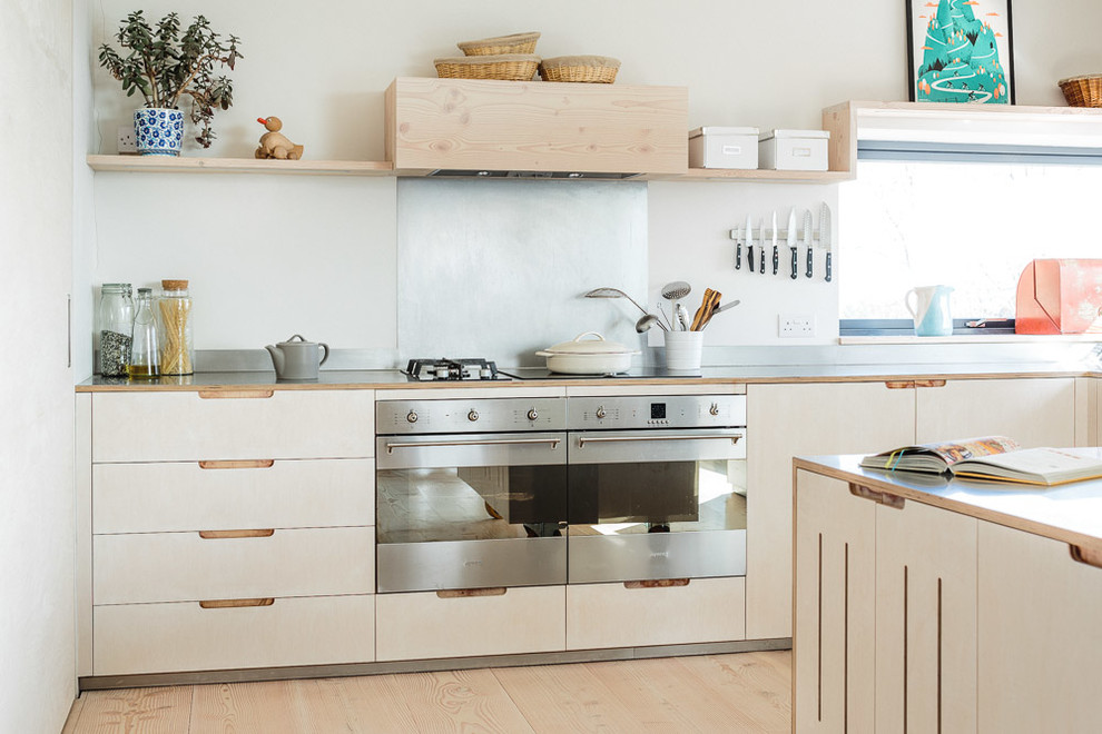 Design ideas for a mid-sized scandinavian l-shaped eat-in kitchen in Other with flat-panel cabinets, light wood cabinets, stainless steel benchtops, metallic splashback, stainless steel appliances, light hardwood floors, with island and a farmhouse sink.