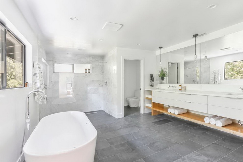 This is an example of a large modern master bathroom in Sacramento with flat-panel cabinets, white cabinets, a freestanding tub, a double shower, a two-piece toilet, gray tile, white tile, marble, white walls, slate floors, an undermount sink, grey floor, an open shower and white benchtops.