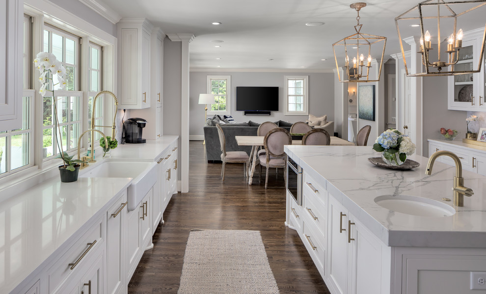 This is an example of a large transitional open plan kitchen in Nashville with a farmhouse sink, shaker cabinets, white cabinets, marble benchtops, stainless steel appliances, dark hardwood floors, with island and brown floor.